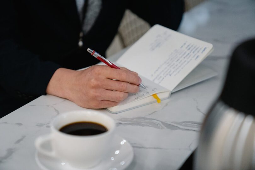 close up of a man writing in his calendar and drinking coffee