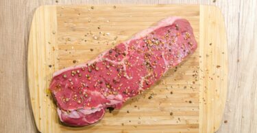 flat lay photography of slice of meat on top of chopping board sprinkled with ground peppercorns