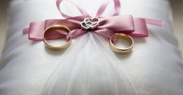 selective focus photography of silver colored engagement ring set with pink bow accent on throw pillow