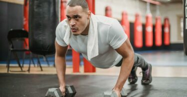 muscular ethnic sportsman performing push ups with dumbbells in gym