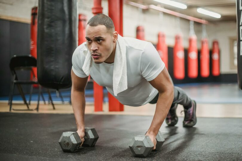 muscular ethnic sportsman performing push ups with dumbbells in gym