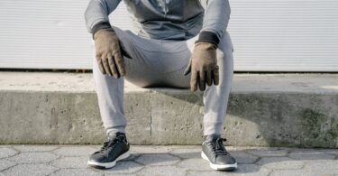 crop faceless man in gray outfit sitting on curb