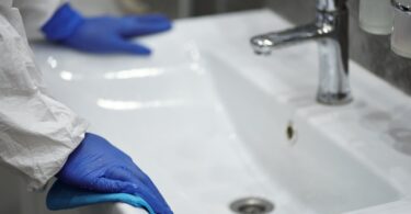 person in latex gloves cleaning washbasin